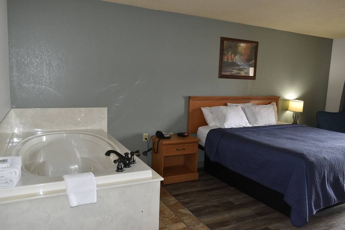 Une chambre d’hôtel avec une baignoire, un lit recouvert d’une courtepointe bleue, une table de chevet avec une lampe et un tableau accroché au mur.