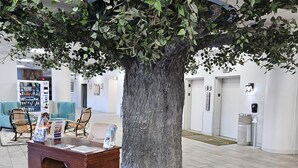 Un hall d’entrée avec un grand arbre artificiel, un espace détente et un distributeur de billets.