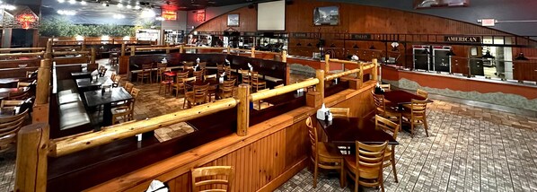 Un restaurante con cabinas, mesas, una barra y letreros que indican cocina de 'Steaks', mariscos, italiana y americana.