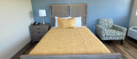 A bedroom with a large bed, a nightstand, a chair, and a wall-mounted air conditioning unit.