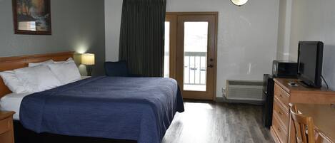 Ein Hotelzimmer mit einem großen Bett, einem Schreibtisch mit Fernseher, einem Schminktisch und einem Fenster mit Vorhängen, sowie einem Bild an der Wand.