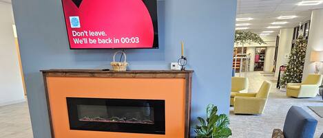 A modern lobby with a fireplace, comfortable seating, and a television displaying a message.
