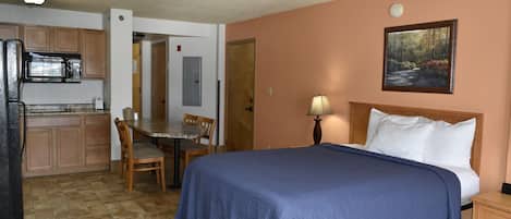 Habitación de hotel con cama, escritorio, silla, lámpara y un cuadro en la pared.