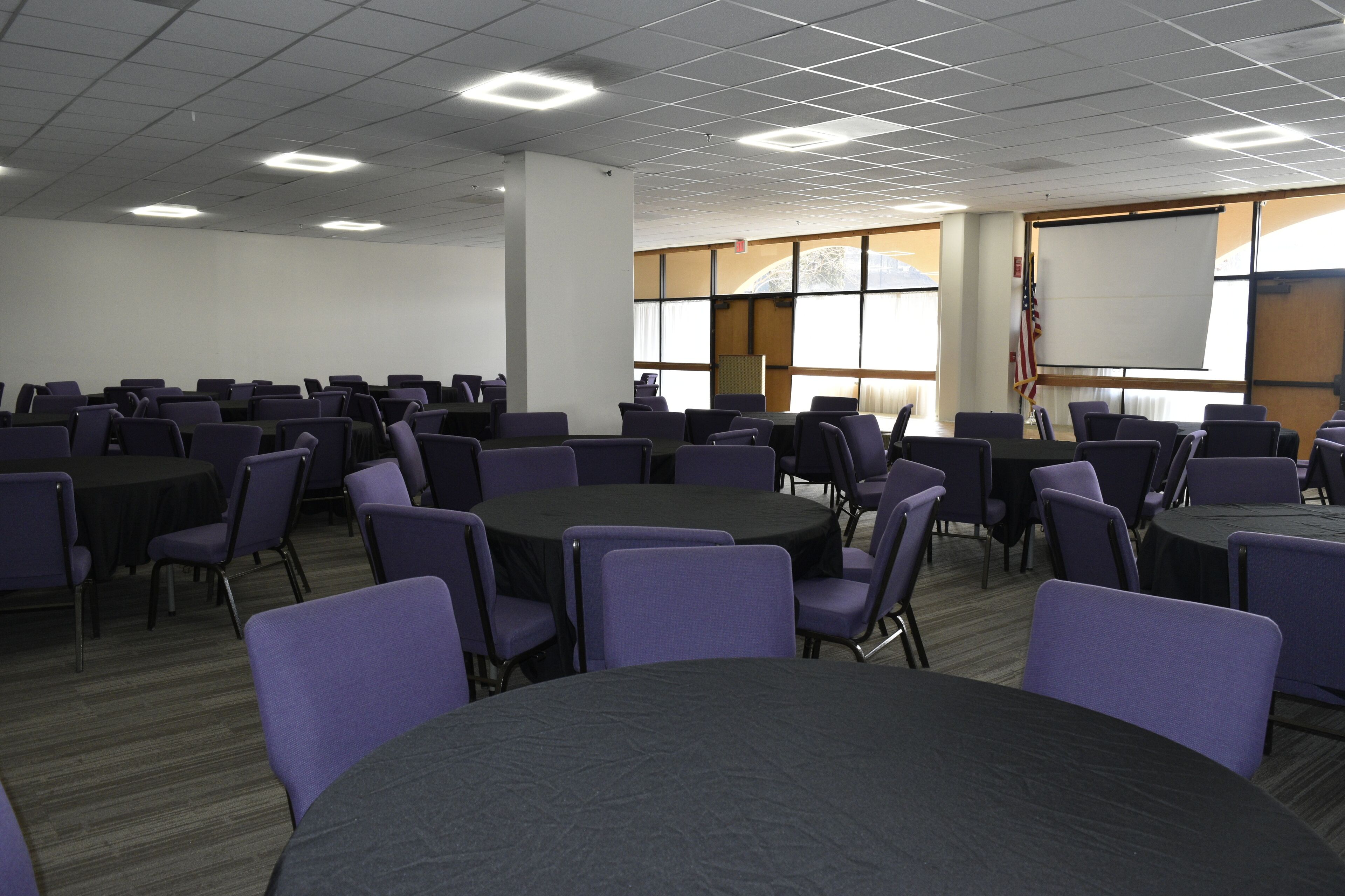 Une salle de conférence dotée de plusieurs tables rondes et de chaises, de grandes fenêtres et d’un drapeau américain.