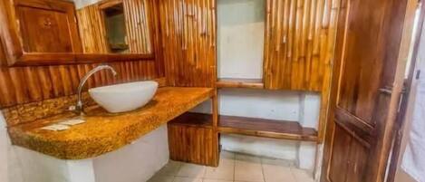 Un baño con tocador de madera, lavamanos y espejo.