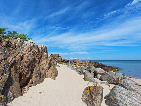 Ein steiniger Küstenpfad führt zum Meer unter klarem Himmel.