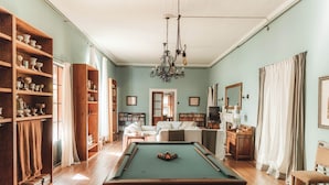 A pool table in a room with wooden floors, bookshelves, a sofa, and a television. - Estancia La Violeta (Chajarí)