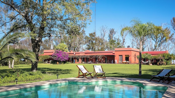 A swimming pool with lounge chairs, a red building, and surrounding greenery. - Estancia La Violeta (Chajarí)
