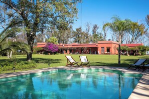 A swimming pool with lounge chairs, a red building, and surrounding greenery. - Estancia La Violeta (Chajarí)