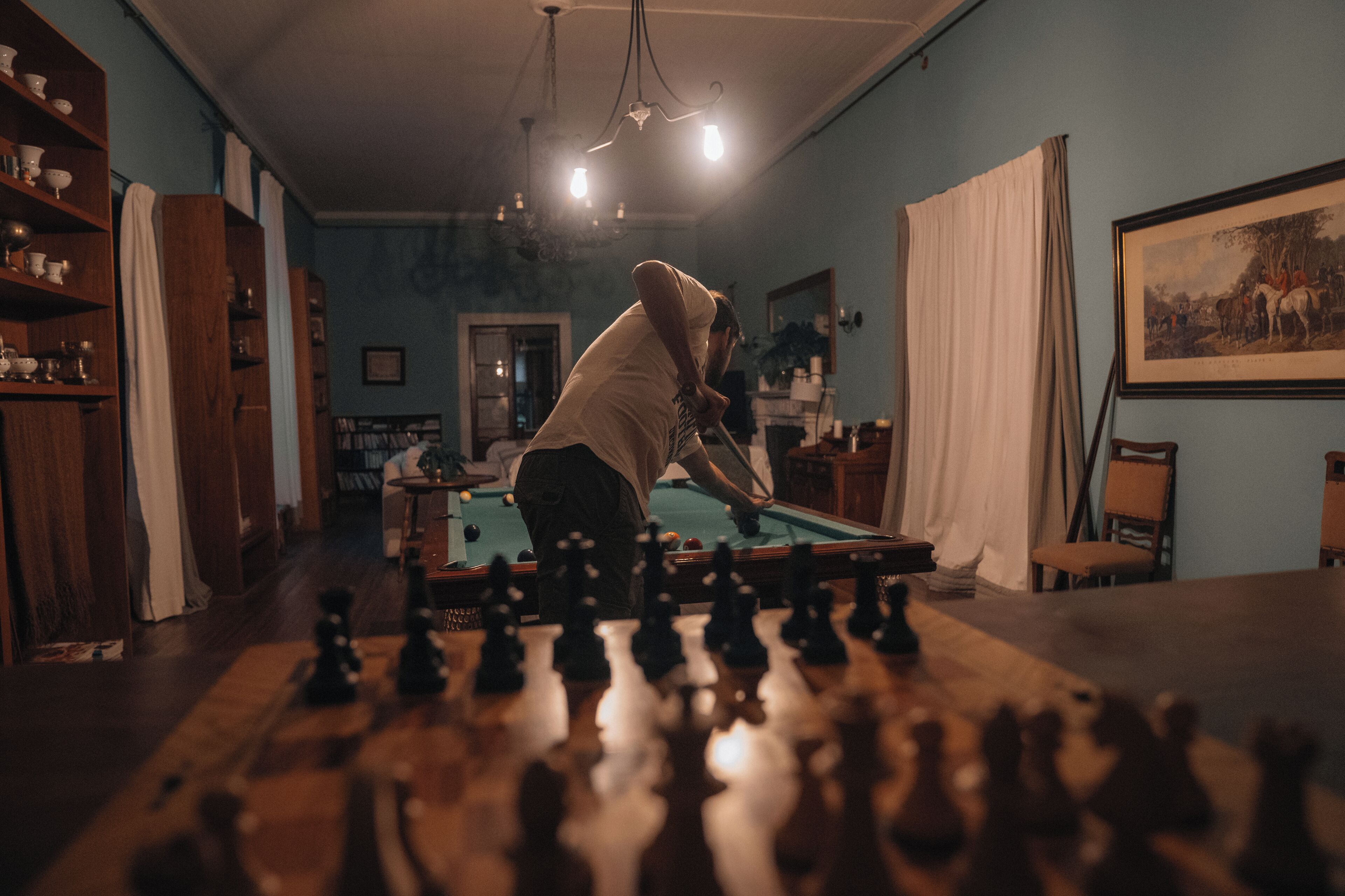 Una persona jugando ajedrez en una habitación con muebles de madera, una mesa de billar y un cuadro en la pared.