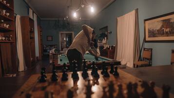 Una persona jugando ajedrez en una habitación con muebles de madera, una mesa de billar y un cuadro en la pared.