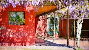 A red building with a glass facade, a covered outdoor area, and a tree with purple flowers. - Estancia La Violeta (Chajarí)