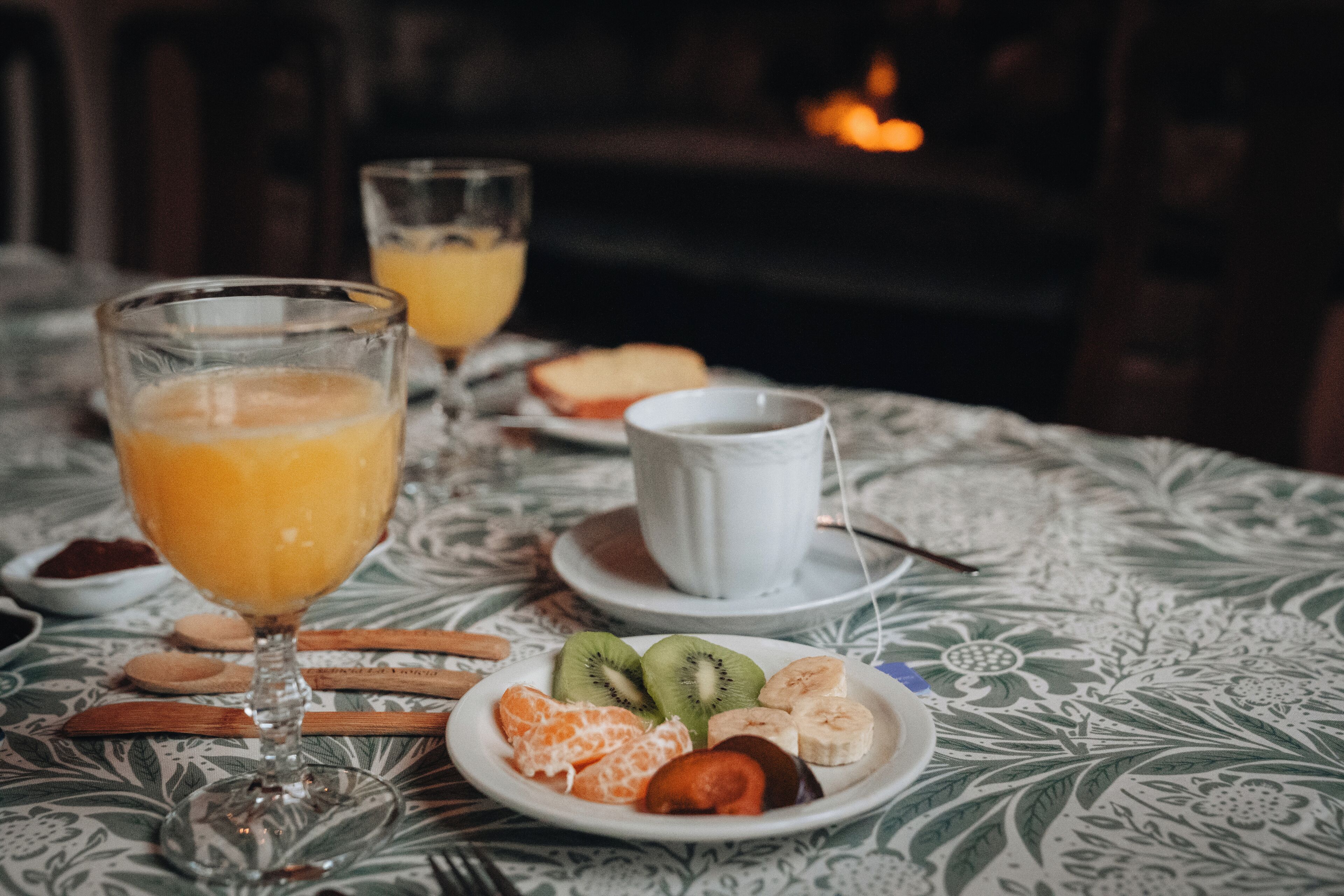 A breakfast setting with a plate of fruit, a glass of orange juice, and a cup of coffee on a table with a patterned tablecloth.