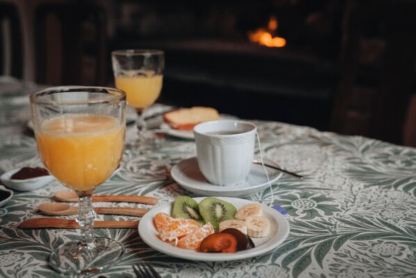 Una mesa con mantel estampado, con un plato de fruta, un vaso de zumo de naranja y una taza de café.