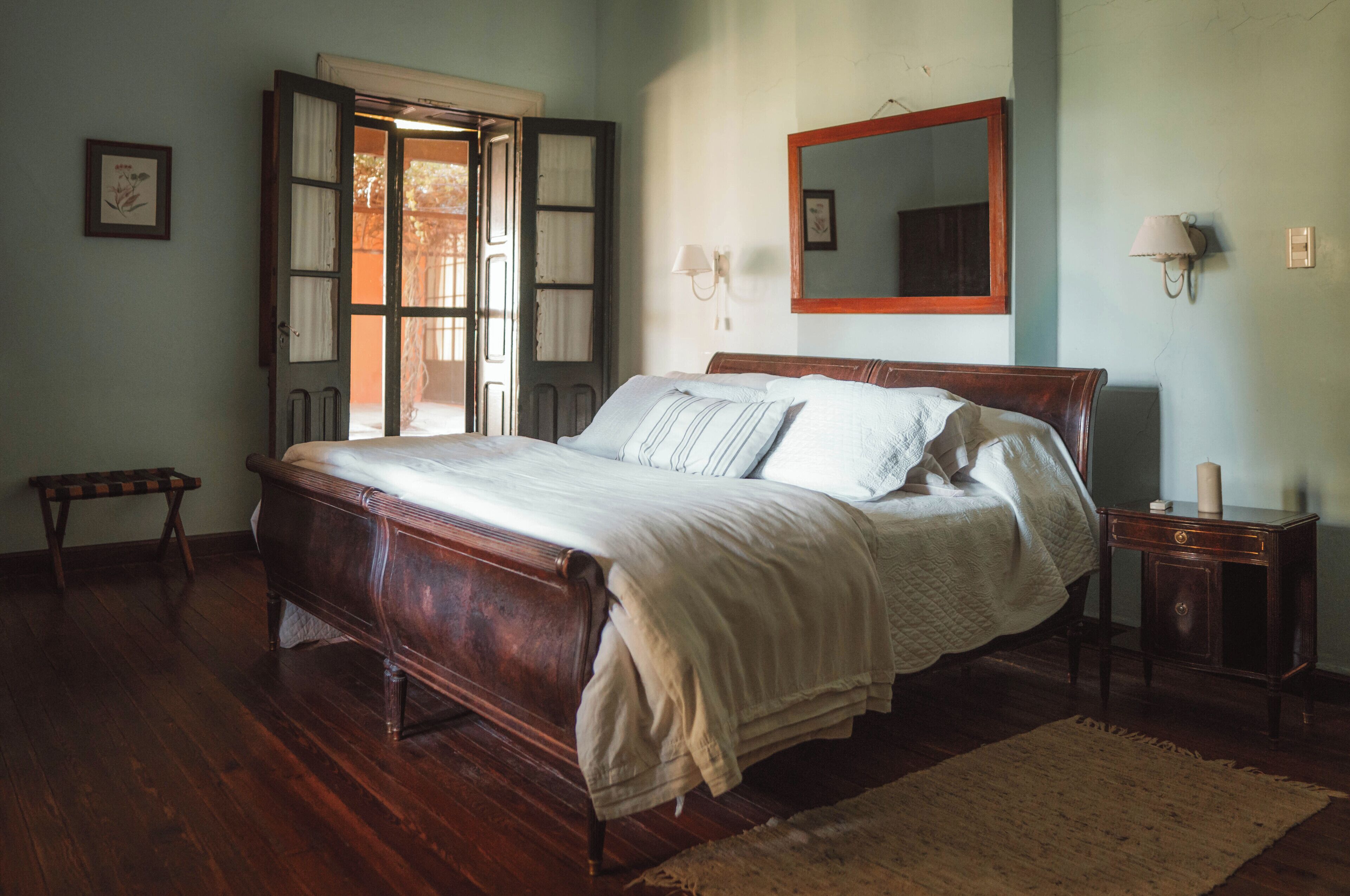 A traditional bedroom with a wooden bed, a bench, a bedside table, and a mirror on the wall.