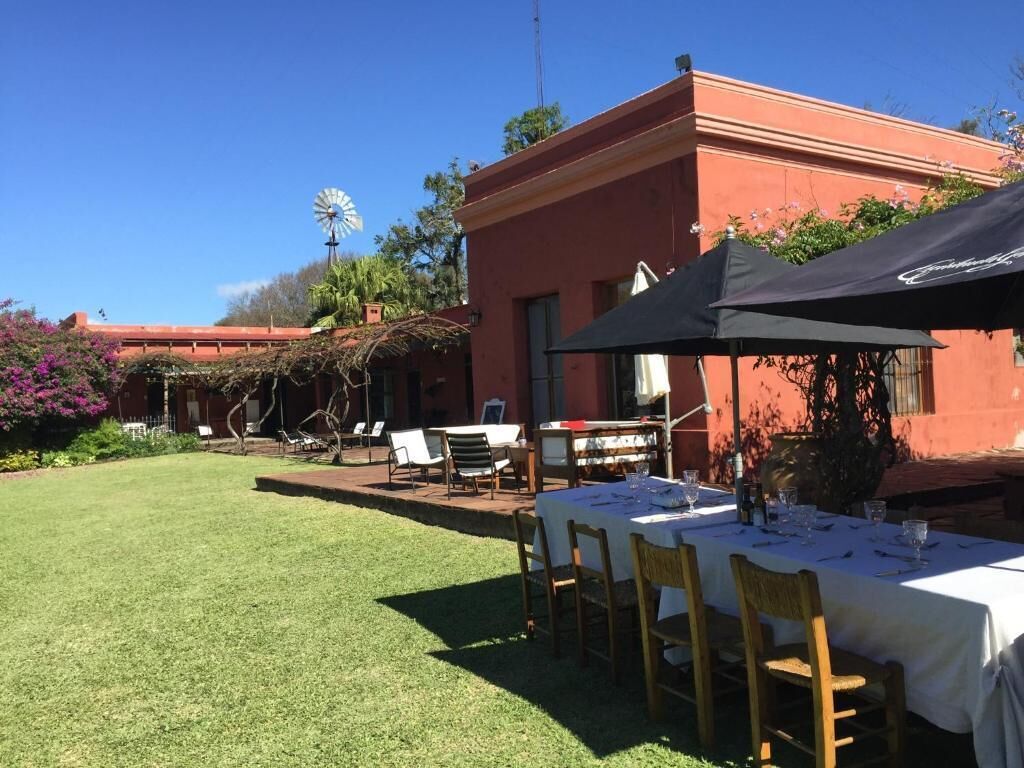 Un área de comedor al aire libre con mesas preparadas para dos, un molino de viento y un edificio de fachada roja.