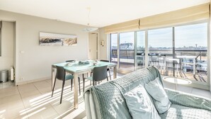 A modern living room with a large glass door leading to a balcony, a dining area with a table and chairs, and a cozy seating area with a sofa. - Apartment Near Oostduinkerke Nature Reserve (Koksijde)