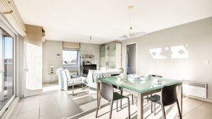 A modern living room with a glass dining table, a sofa, and a large window. - Apartment Near Oostduinkerke Nature Reserve (Koksijde)