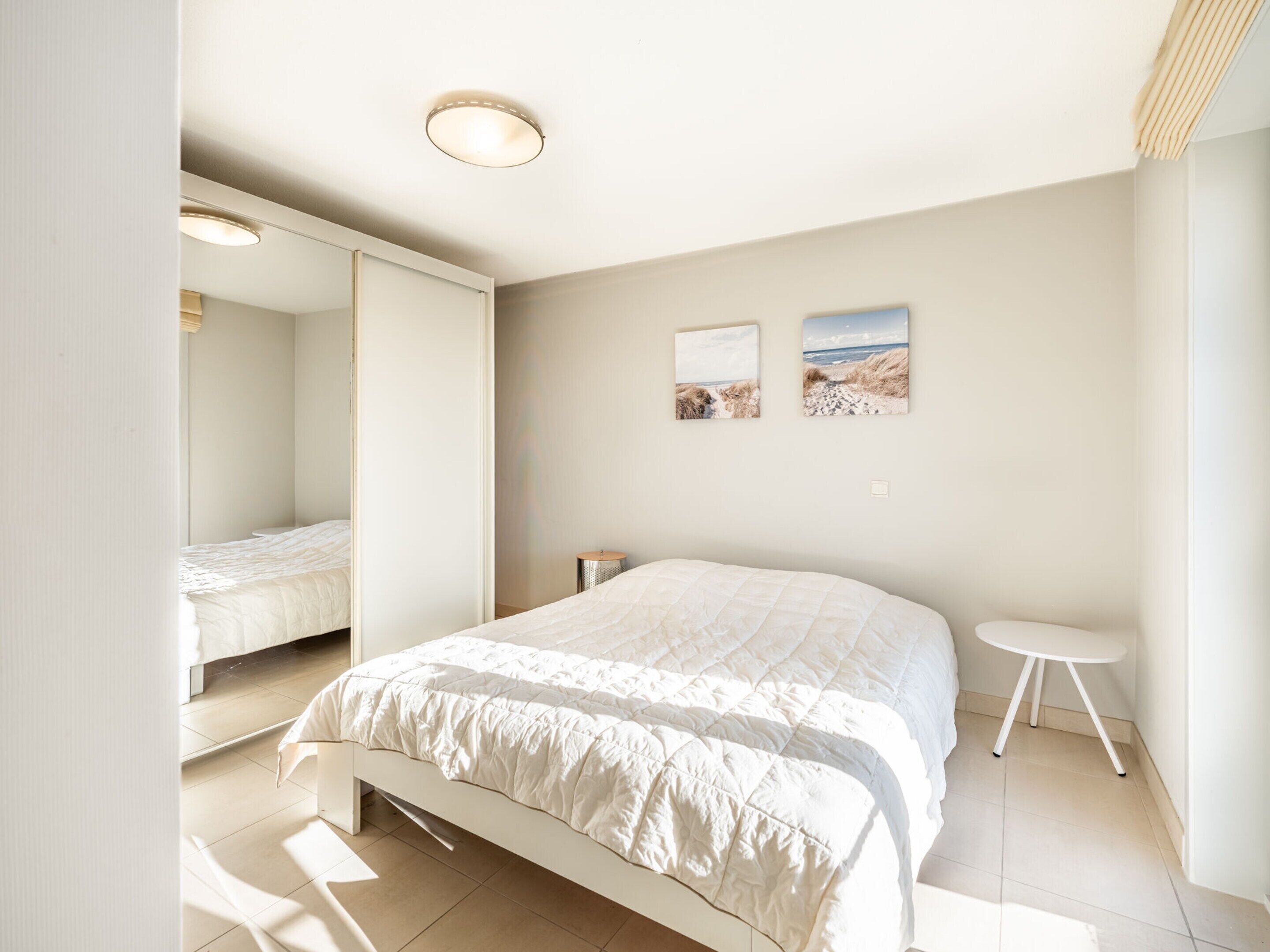 A bedroom with a bed, a small bedside table, a mirror, and two wall-mounted pictures.