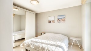 A bedroom with a bed, a small bedside table, a mirror, and two wall-mounted pictures. - Apartment Near Oostduinkerke Nature Reserve (Koksijde)