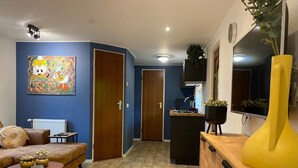 Een woonkamer met een bank, salontafel en een schilderij aan de muur. Er is een houten kast en een gele vaas met een plant.