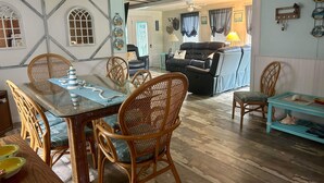 A dining area with a glass-top table and wicker chairs, a living room with a sofa and a coffee table, and a hallway leading to another room.