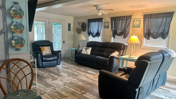 A living room with a black leather sofa, a black armchair, a wooden chair, and a small table with a lamp.