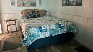 A bedroom with a bed, a nightstand, a window with blinds, and two wall-mounted paintings.