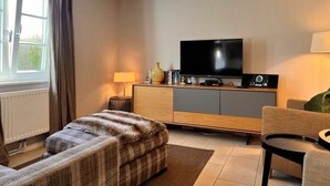 Una sala de estar moderna con una televisión de pantalla plana, un sofá, una butaca y una lámpara.