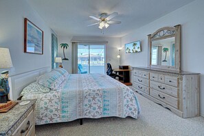 A bedroom with a bed, dresser, ceiling fan, and a view through the window.