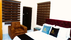 Una habitación de hotel con una cama, un sillón marrón y dos ventanas con persianas.
