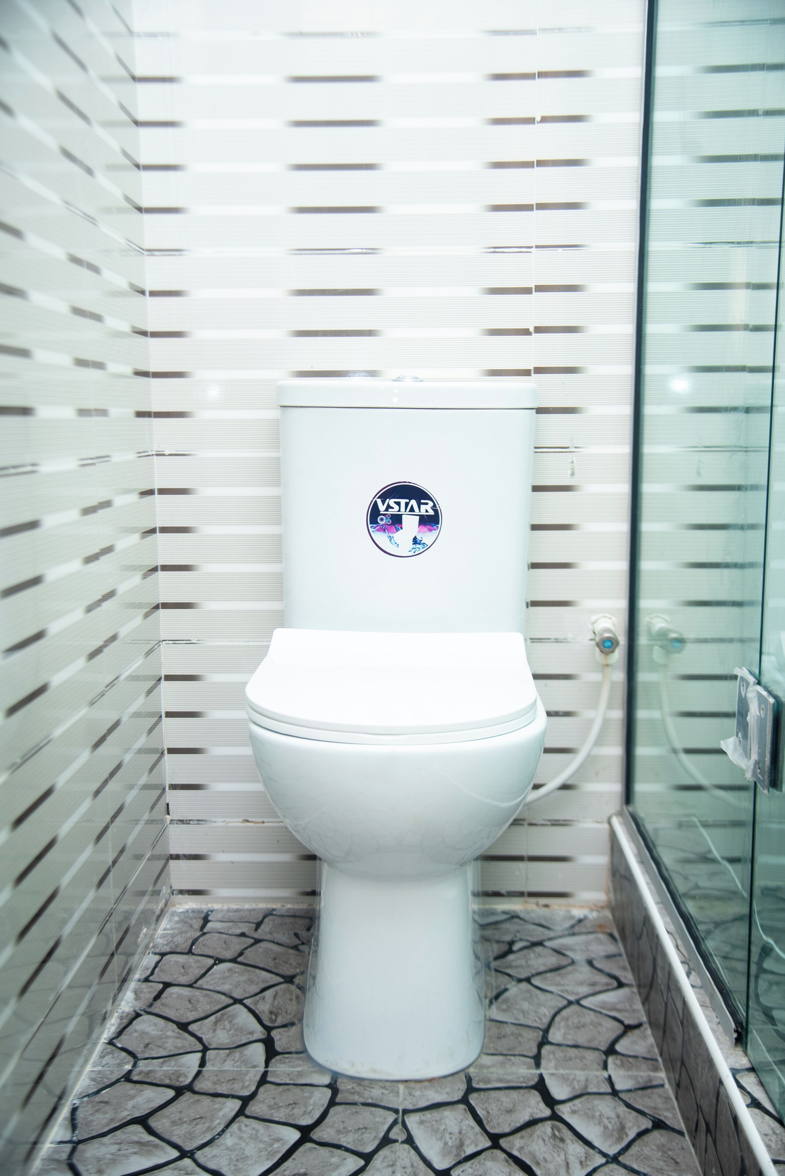 A white toilet with a sticker, a tiled floor, and a glass shower enclosure.