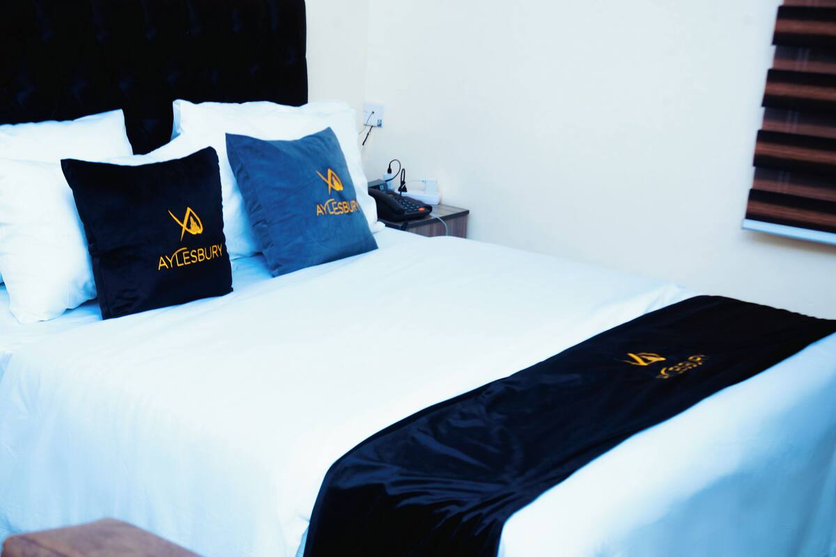 Ein ordentlich bezogenes Bett mit weißen Leinentüchern und zwei schwarzen Kissen mit einem Logo.