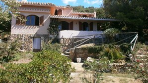 A two-story house with a stone foundation, a tiled roof, and a small garden area with various plants and a stone wall. - Donata Comfortable Holiday Residence (Maracalagonis)