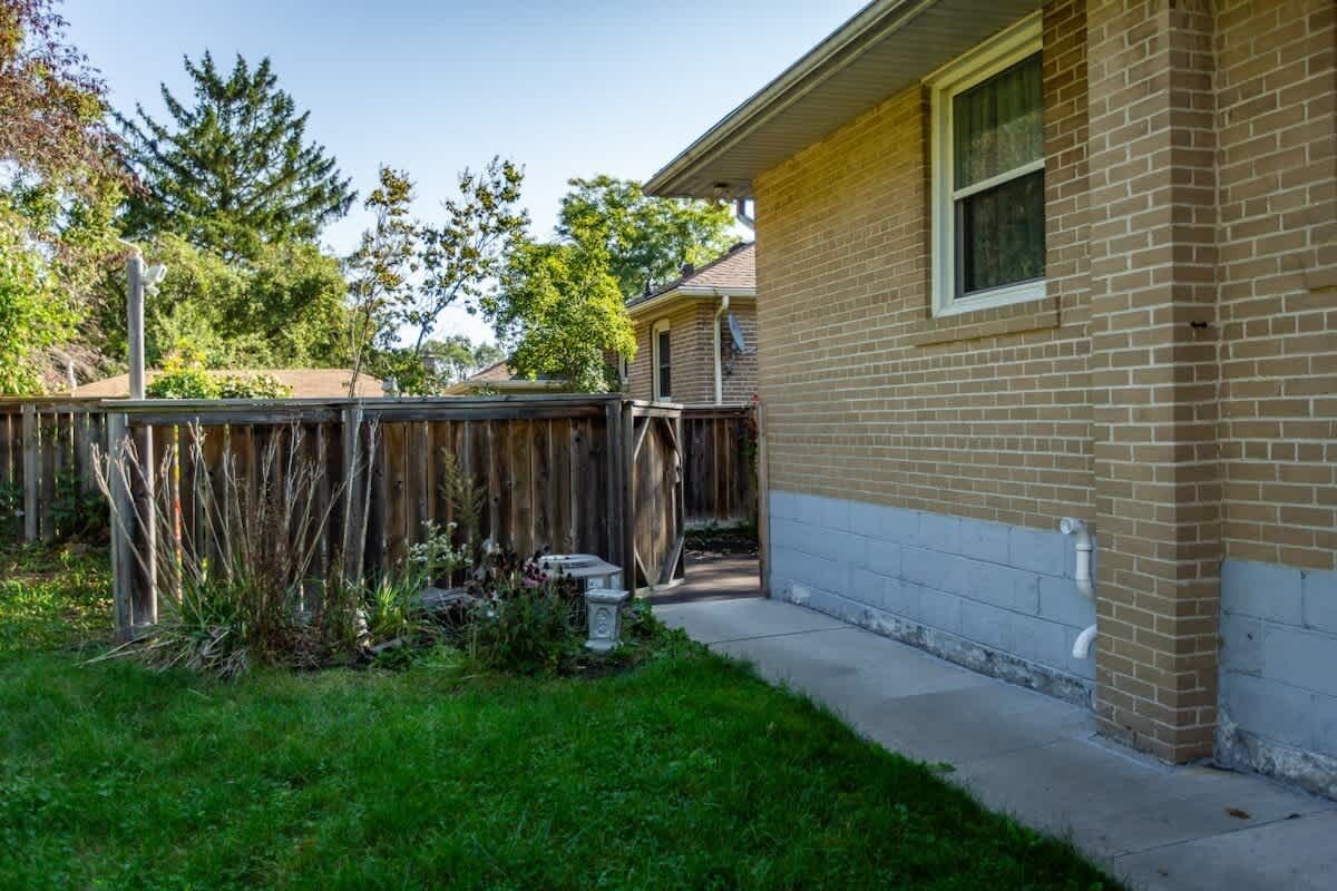 A residential backyard with a wooden fence, a brick house, and a grassy area.