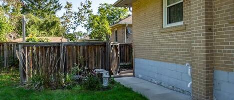A residential backyard with a wooden fence, a brick house, and a grassy area.