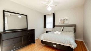 A bedroom with a bed, a dresser, a ceiling fan, a window with curtains, and a wall-mounted picture.