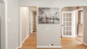 A hallway with a painting of a Parisian street scene, white walls, and wooden flooring.