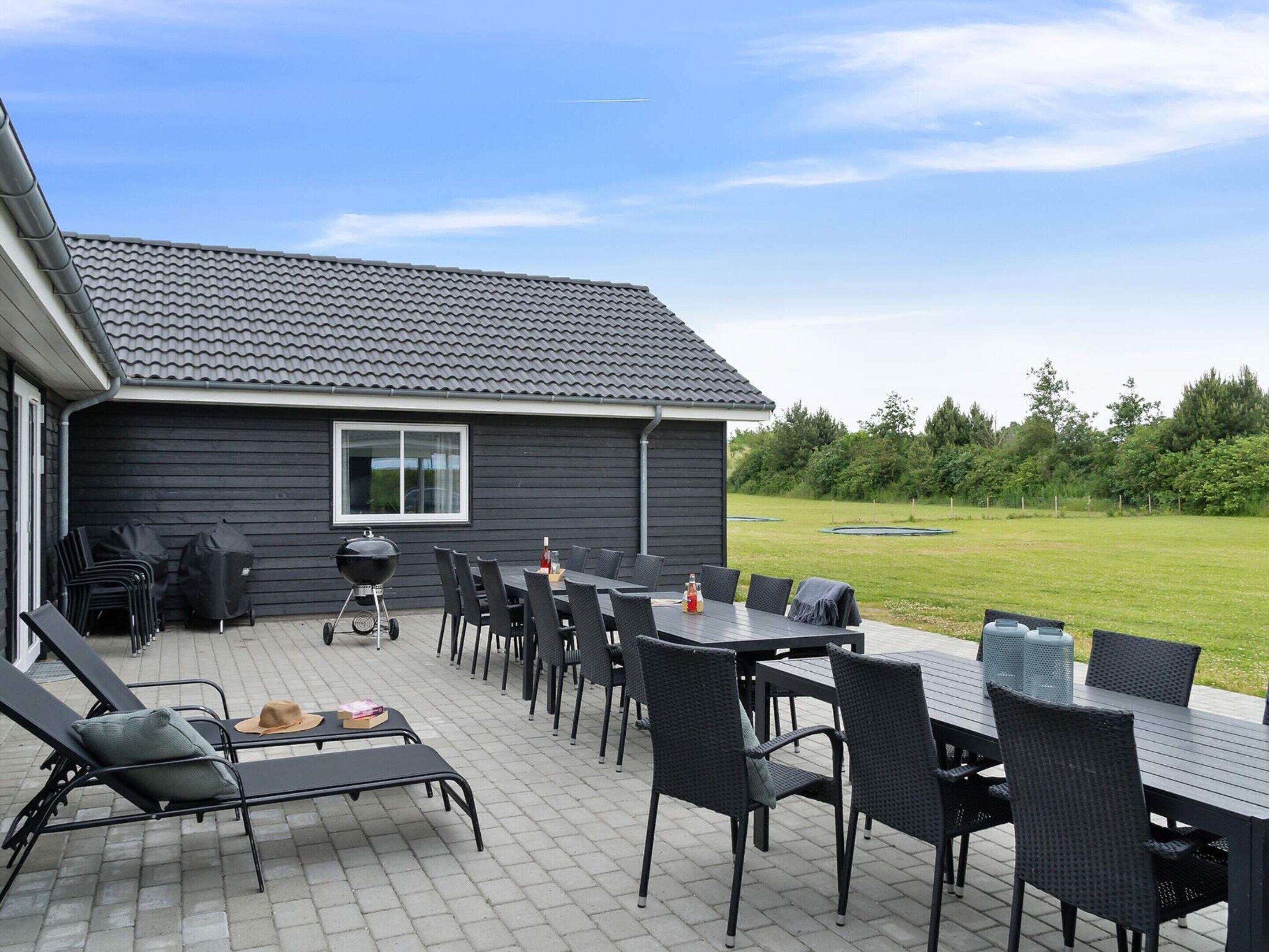 An outdoor patio with a grill, dining table, and lounge chairs.