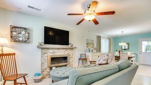Una sala de estar con chimenea, ventilador de techo, televisor y sofá azul claro.