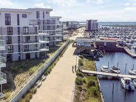 A marina with boats, a walkway, and modern buildings with balconies.