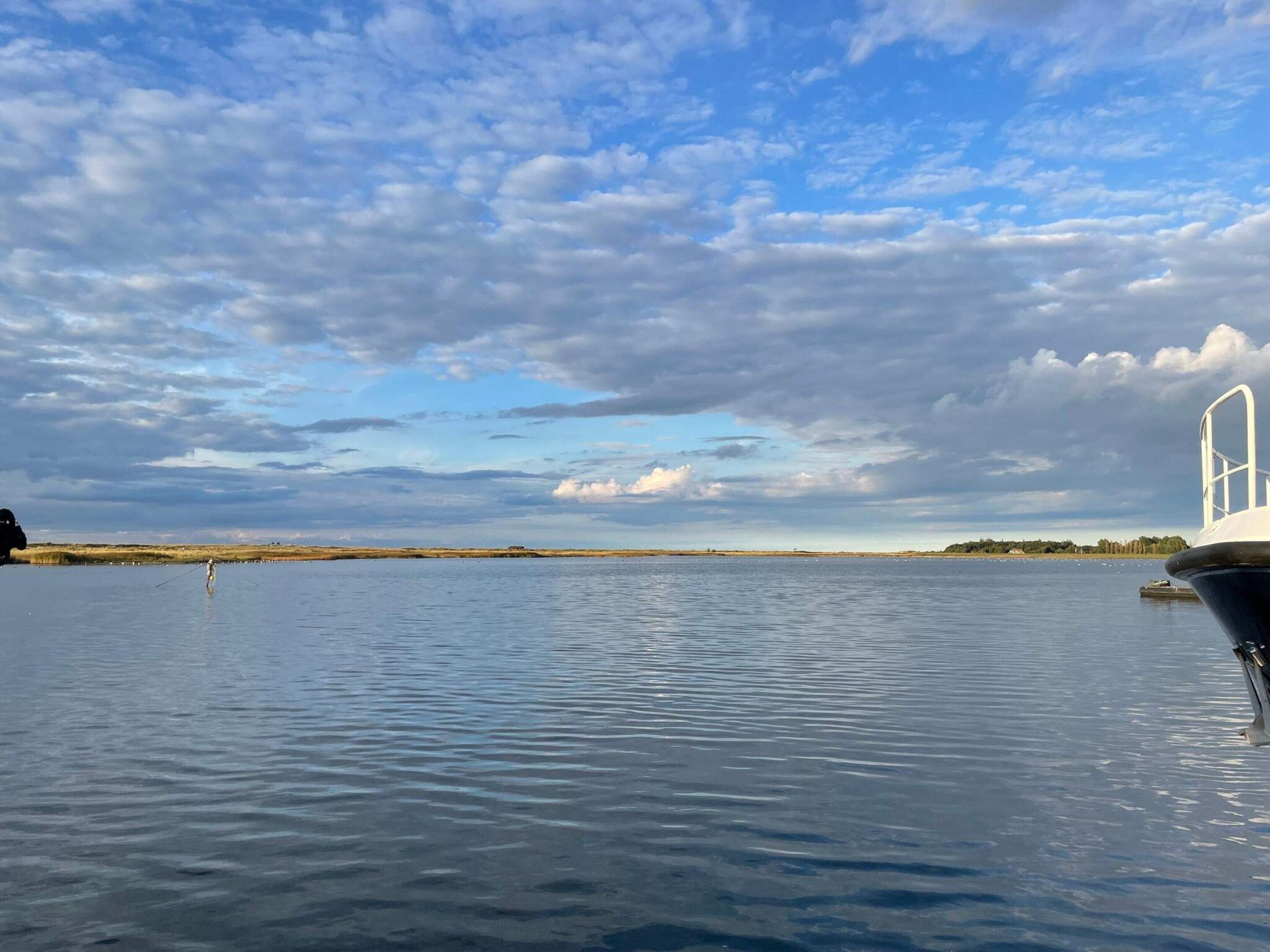 Una masa de agua tranquila con un bote amarrado a la derecha, cielo despejado y una costa lejana.
