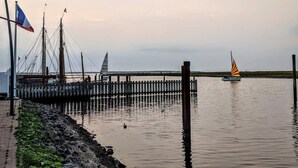 Ein Ufer mit einer Holzsteganlage, Segelbooten und einer Flagge.