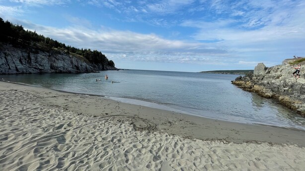 A sandy beach with calm water, rocky cliffs, and a clear sky.