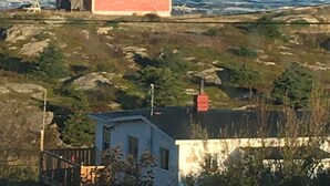 A coastal house with a red exterior, situated on a rocky terrain with waves crashing nearby.