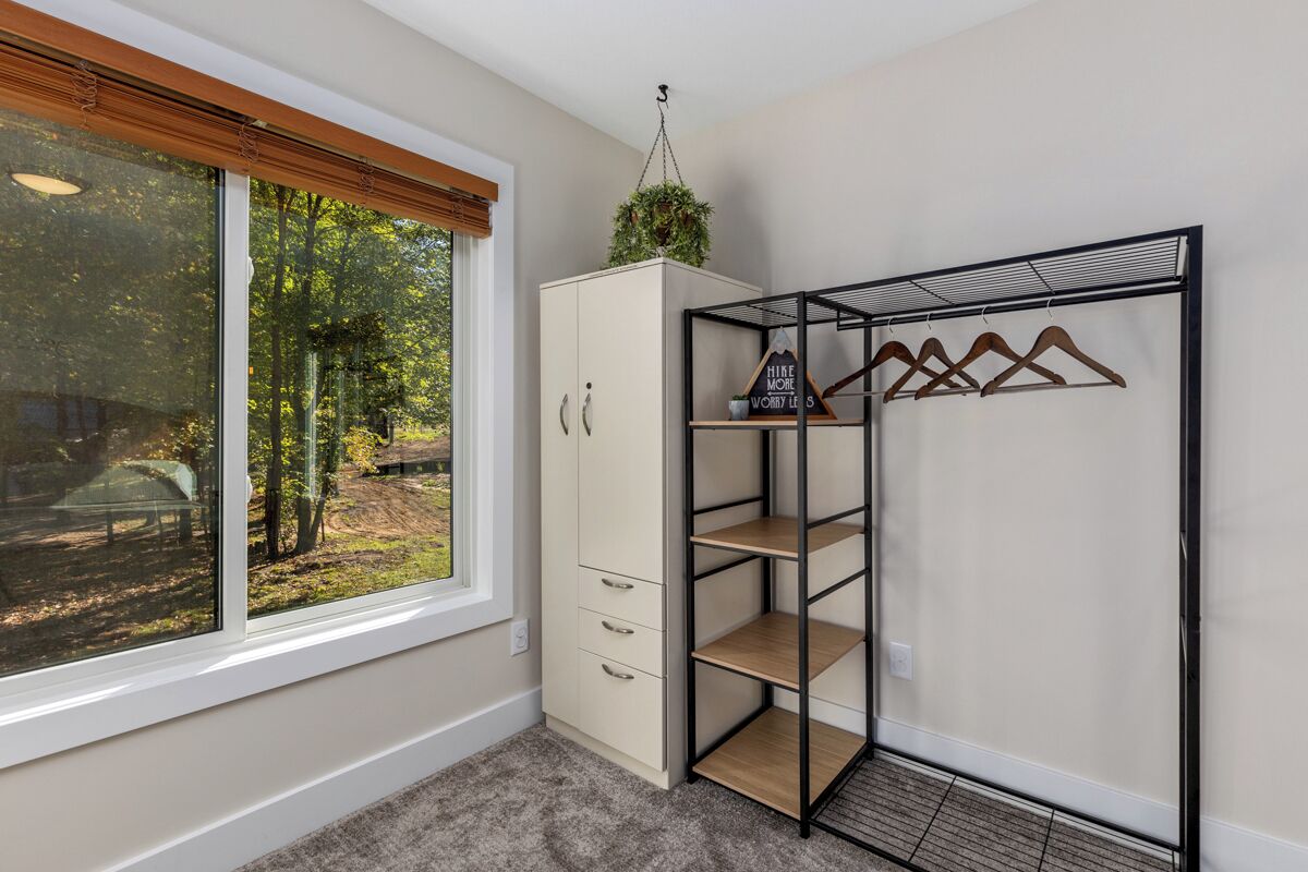Ein Zimmer mit großem Fenster, einem Schrank mit vielen Schubladen und einem Metallregal mit hölzernen Kleiderbügeln.
