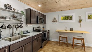 Una cocina moderna con armarios de madera oscura, electrodomésticos de acero inoxidable y una encimera de madera. Hay dos taburetes y una repisa de madera sobre la encimera.