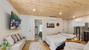 Un dormitorio moderno con techo de madera, cama, sofá, televisor y una mesita con una planta.