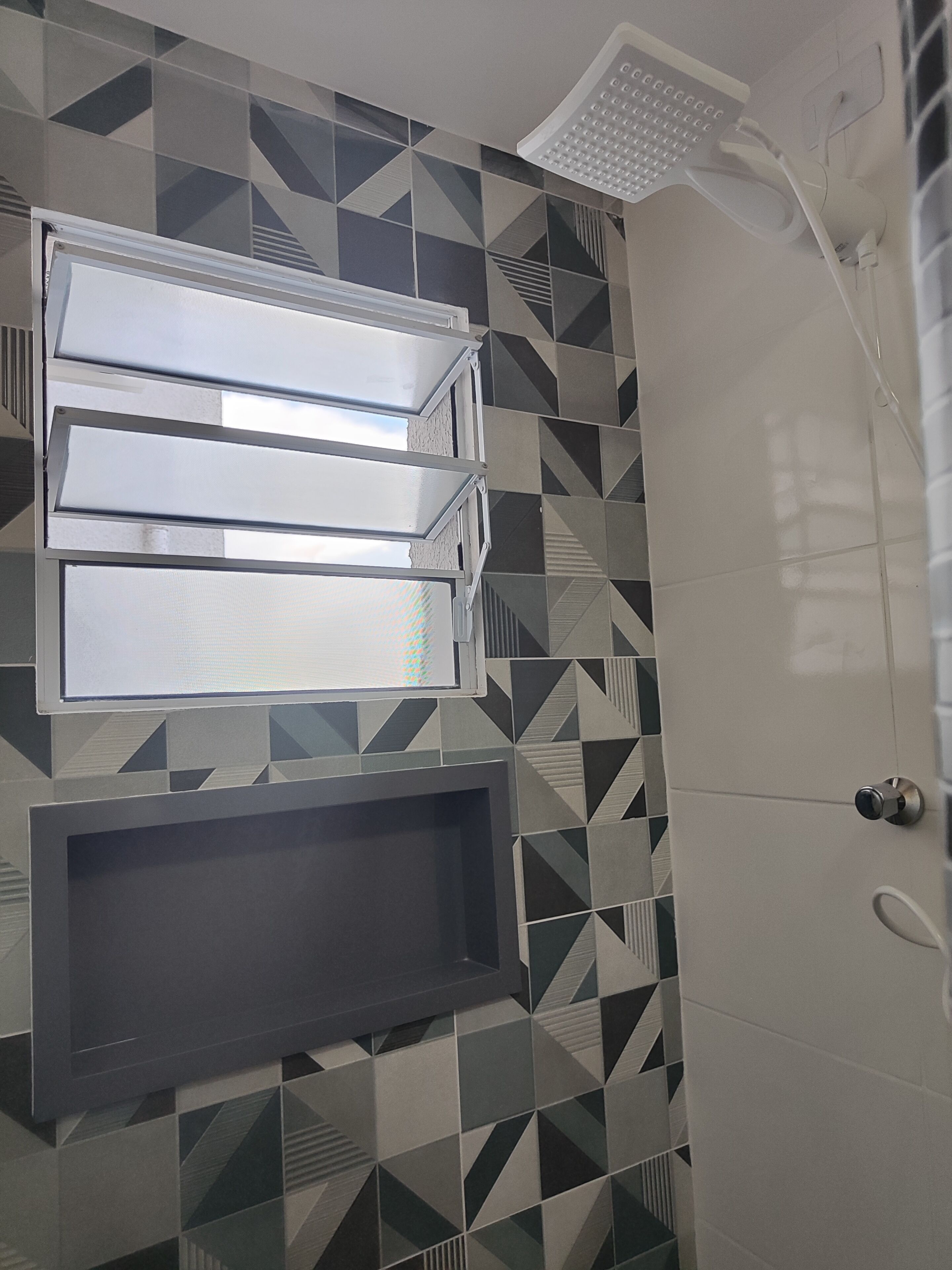 A bathroom with a geometric tile pattern, a built-in shower, and a wall-mounted vanity with a mirror.