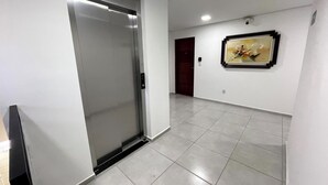 A hallway with a closed elevator, a framed artwork on the wall, and a tiled floor.